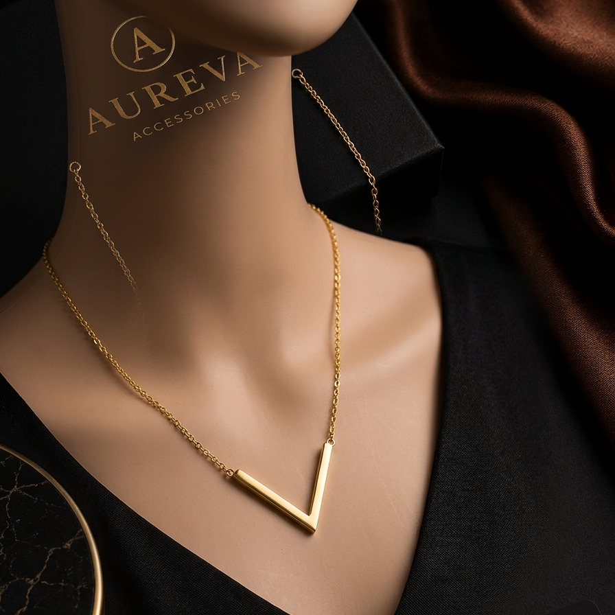 A gold V-shaped pendant necklace displayed on a mannequin torso wearing a black V-neck top, with Aureva Accessories branding visible on the mannequin and packaging.