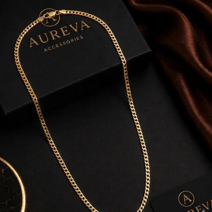 A gold-tone chain necklace draped elegantly over a black Aureva Accessories box, with a dark brown satin fabric and branded cards in the background.
