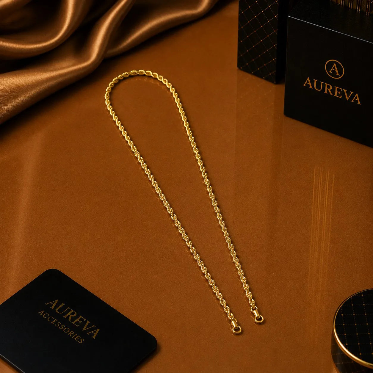 A gold rope chain necklace displayed on a brown satin surface, with Aureva Accessories branded black boxes visible in the background.