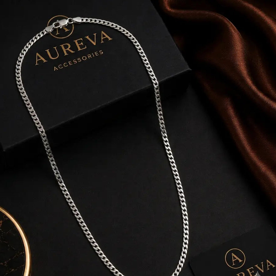 A silver-toned curb chain necklace draped over black Aureva Accessories boxes with a brown satin fabric in the background.