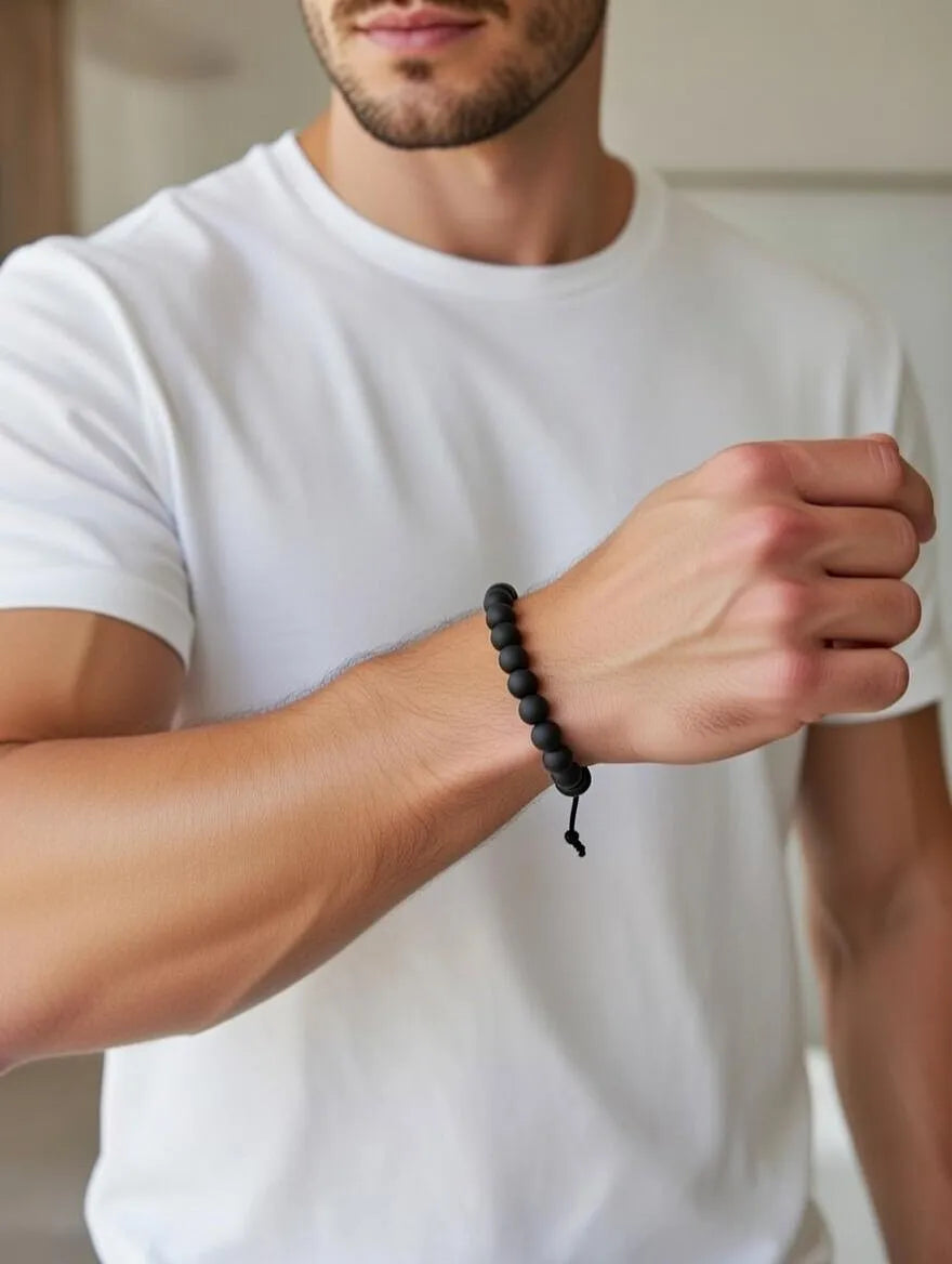 Unisex matte black onyx beaded bracelet with an adjustable black cord closure displayed on a soft white fabric background.