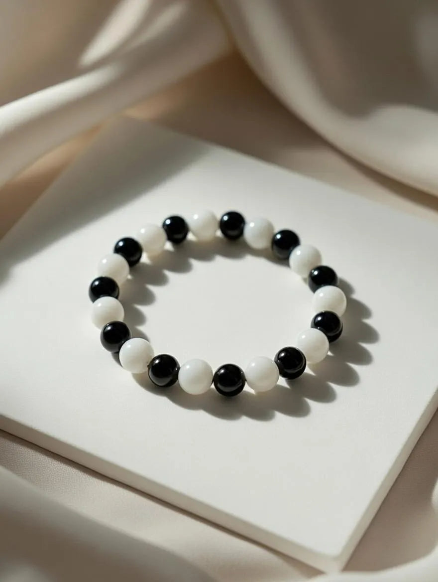 Unisex stretch bracelet featuring alternating polished black and white round beads, displayed on a soft white draped fabric background.