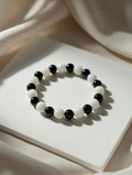 Unisex stretch bracelet featuring alternating polished black and white round beads, displayed on a soft white draped fabric background.