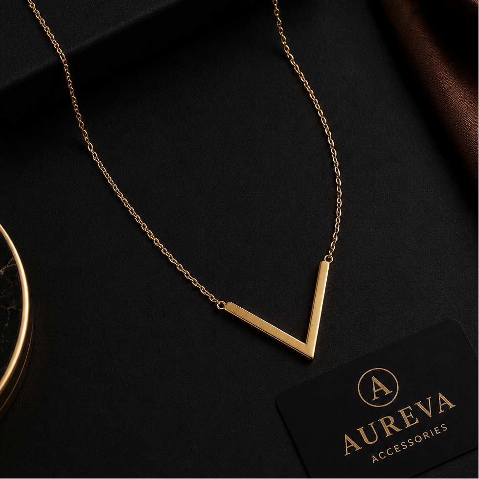 A gold V-shaped pendant necklace on a delicate chain, displayed on a black background with the Aureva Accessories brand box, a brown satin fabric, and a branded card.