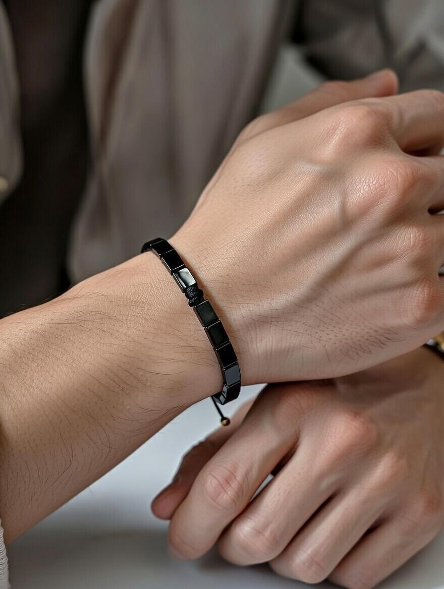 Close-up of a person wearing a black beaded bracelet on a neutral background