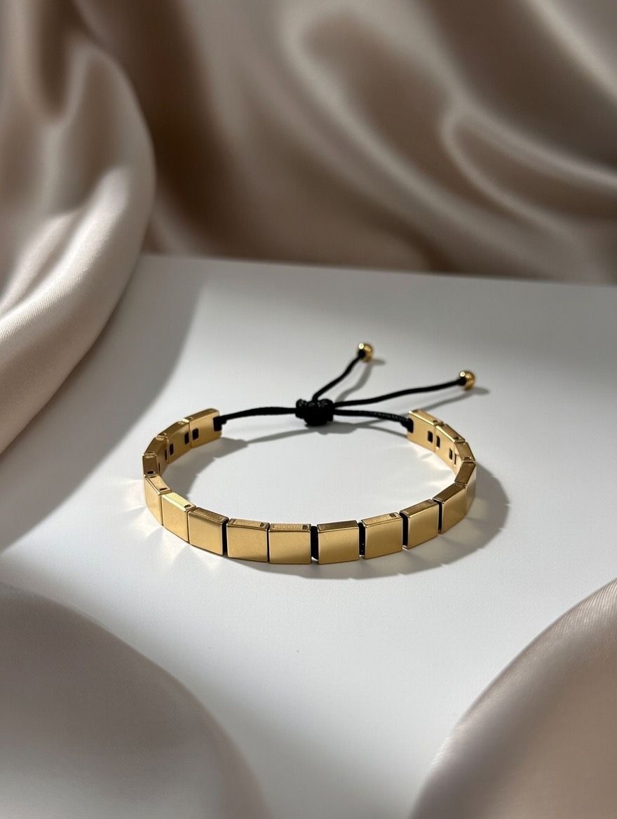 Gold bracelet with black cord on a white surface
