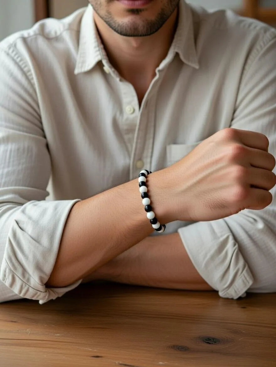 Unisex stretch bracelet featuring alternating polished black and white round beads, displayed on a soft white draped fabric background.