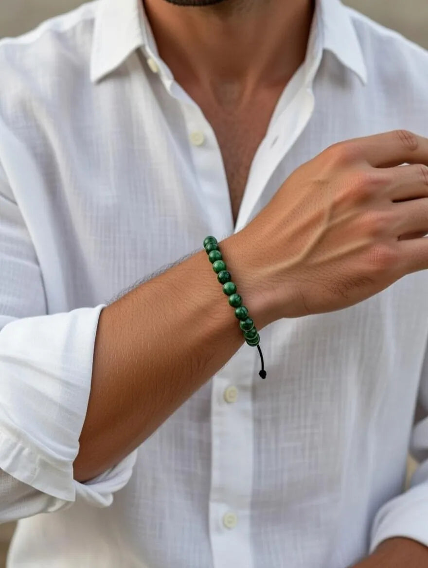 Unisex adjustable bracelet featuring polished green jasper beads with black marbled patterns, displayed on a white surface with elegant neutral fabric draping.