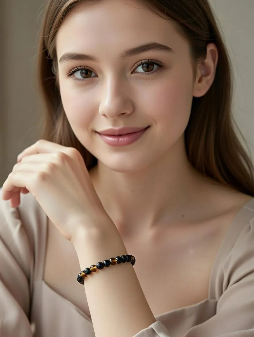 Unisex adjustable bracelet with green obsidian beads and faceted amber-colored tiger eye beads on a black cord, displayed on a white podium with silk fabric.