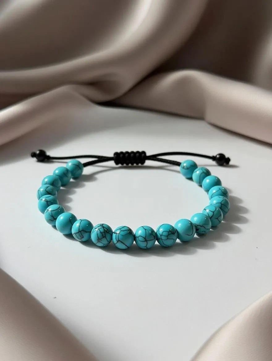 Unisex adjustable bracelet featuring bright turquoise howlite beads with black marble veining, displayed on a white surface with elegant neutral silk draping.