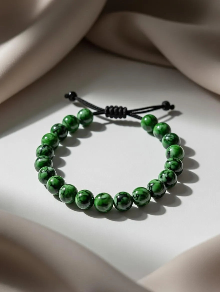 Unisex adjustable bracelet featuring polished green jasper beads with black marbled patterns, displayed on a white surface with elegant neutral fabric draping.