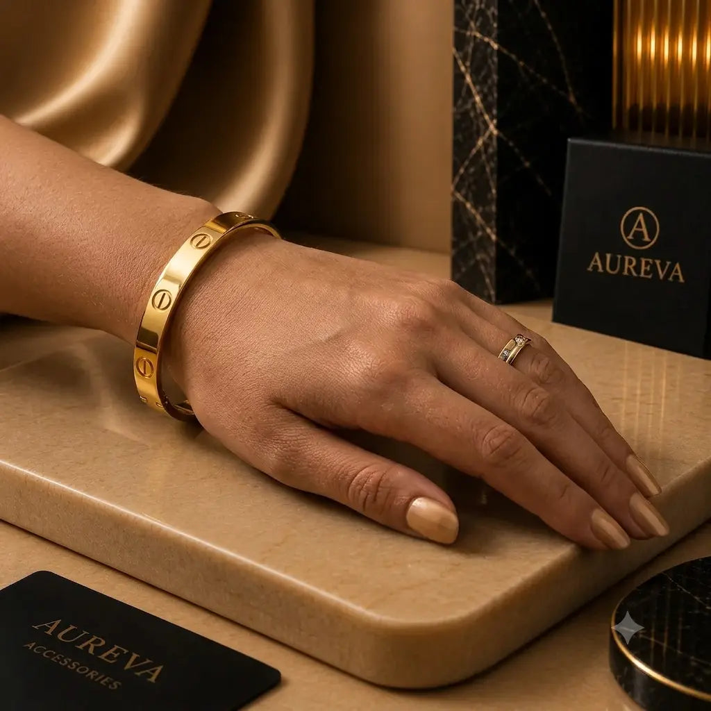 A close-up lifestyle shot of a model's hand wearing a gold bangle bracelet and a gold ring, resting on a beige stone slab. Aureva brand packaging, including a black box and card, is visible in the background.